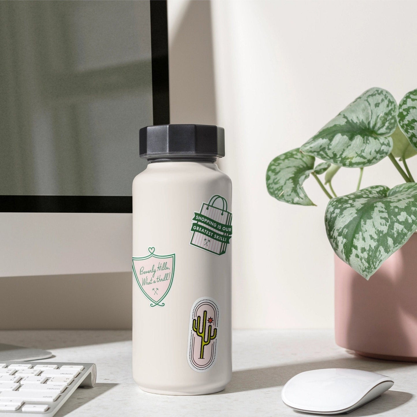 White water bottle with green labels on a desk next to a computer monitor and plant