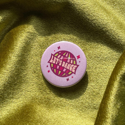 Purple pinback button with a disco ball and 'Let's Dance' text on a green fabric background