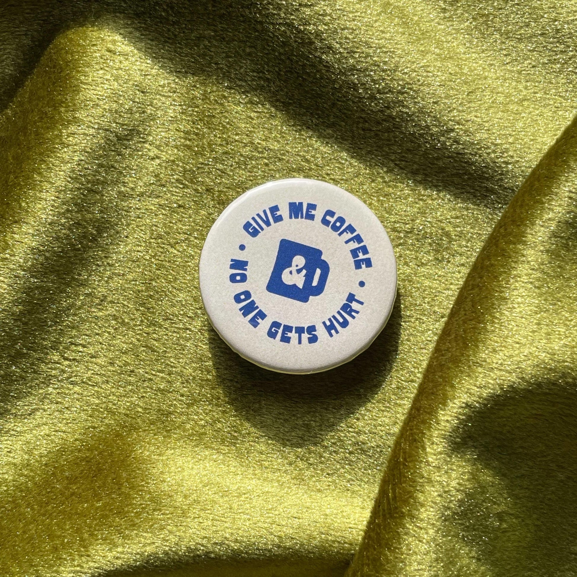close up of pinback button that says Give Me Coffee & No One Gets Hurt in a funky blue font and a blue coffee mug silhouette in the center