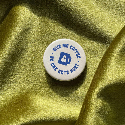 close up of pinback button that says Give Me Coffee & No One Gets Hurt in a funky blue font and a blue coffee mug silhouette in the center