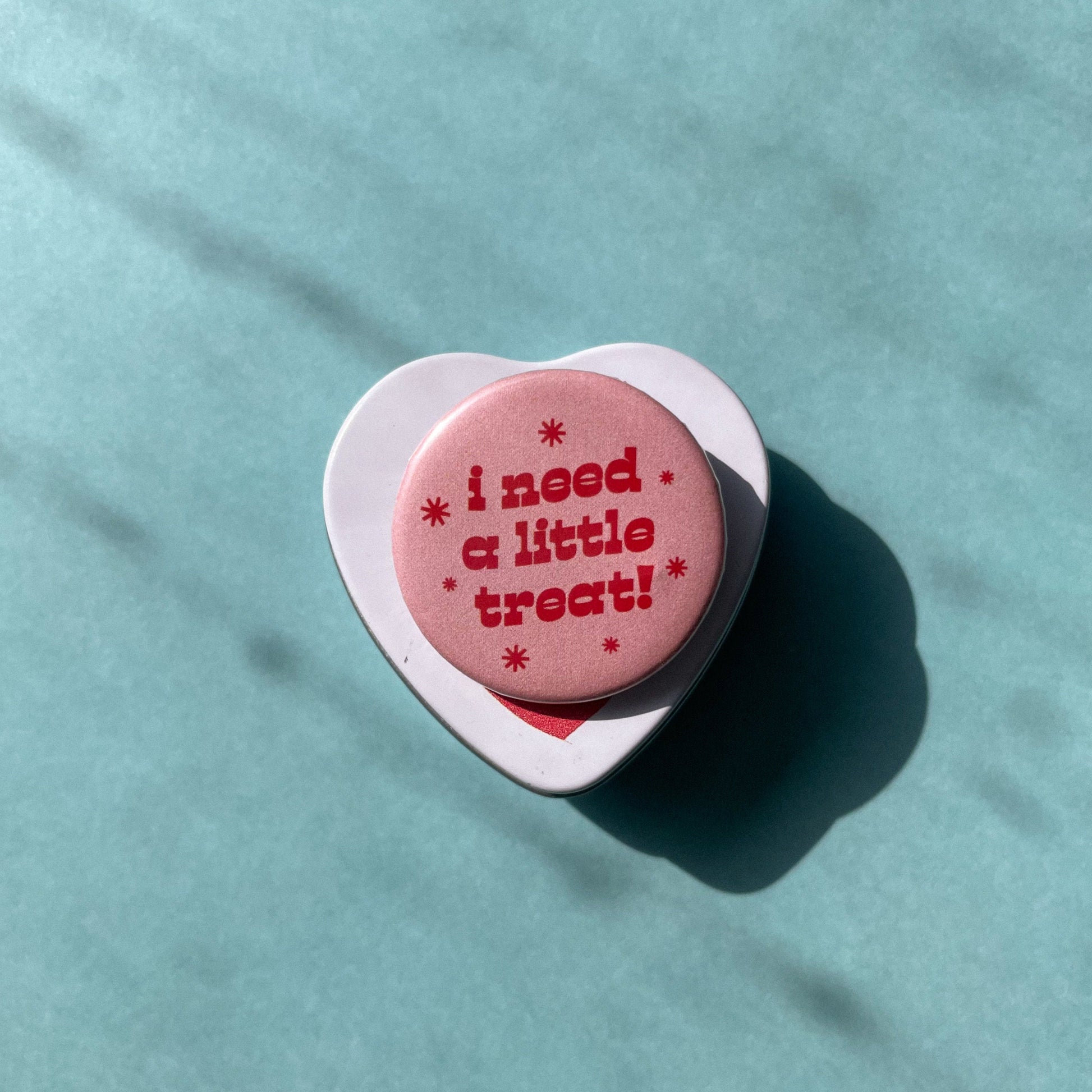 Pink round button with 'i need a little treat!' text on a light blue background