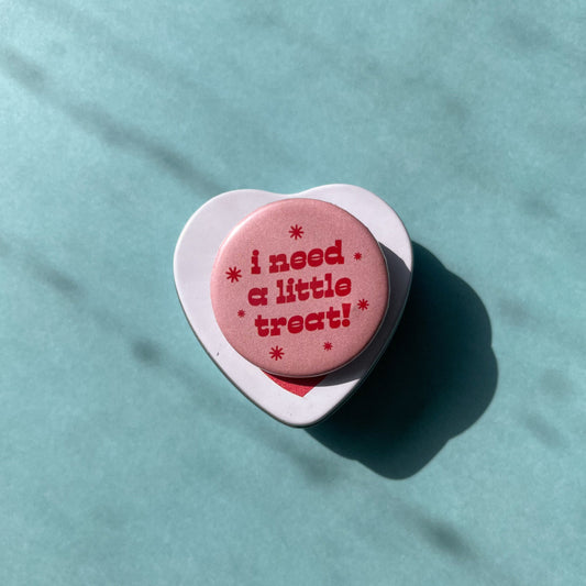 Pink round button with 'i need a little treat!' text on a light blue background