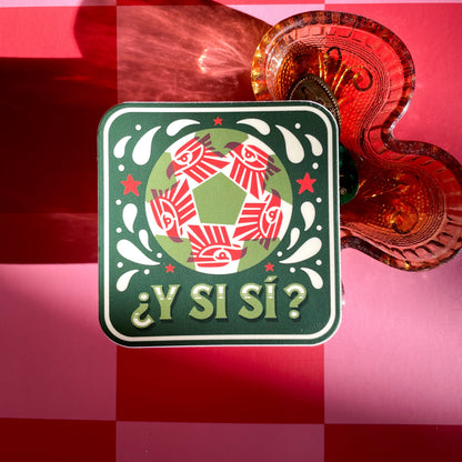 A square sticker with a red, white, and green soccer ball. A red geometric eagle pattern inside the ball, and the Spanish text '¿Y Si Sí?' in green, displayed next to a amber clover-shaped glass tray on a pink and red checkered background.