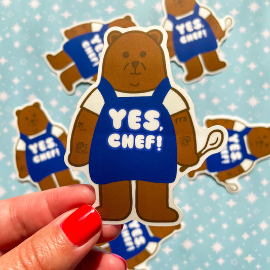 Sticker of a bear wearing a blue apron with 'YES, CHEF!' text on a light blue background.