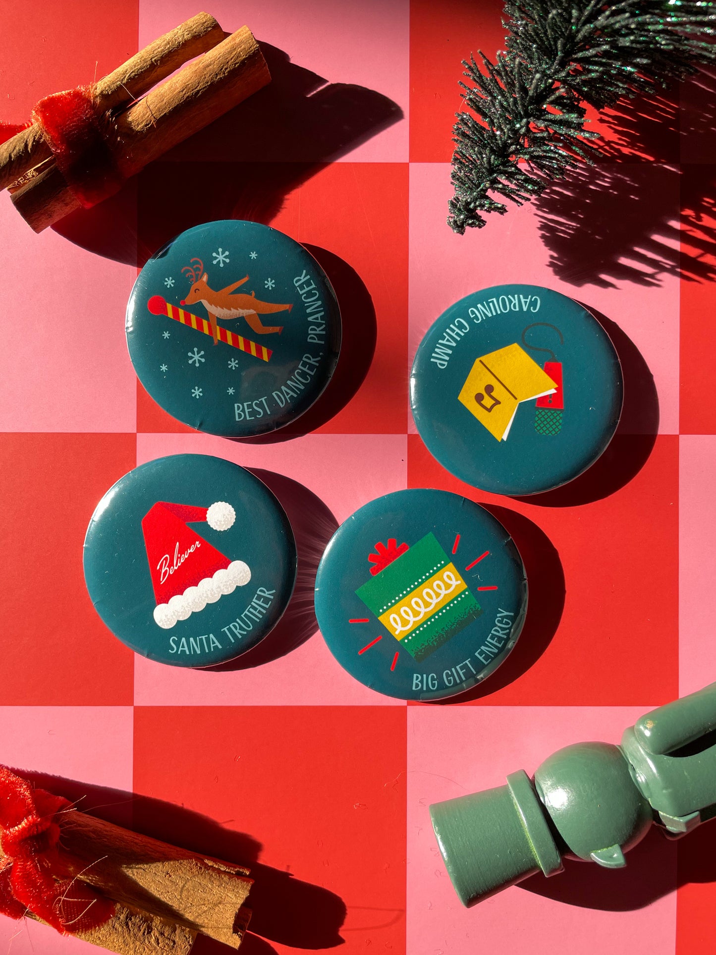 Four Christmas-themed pinback buttons  with superlatives such as best dancer, prancer, santa truther, big gift energy, and caroling champ on a red and pink checkered background with festive decorations.