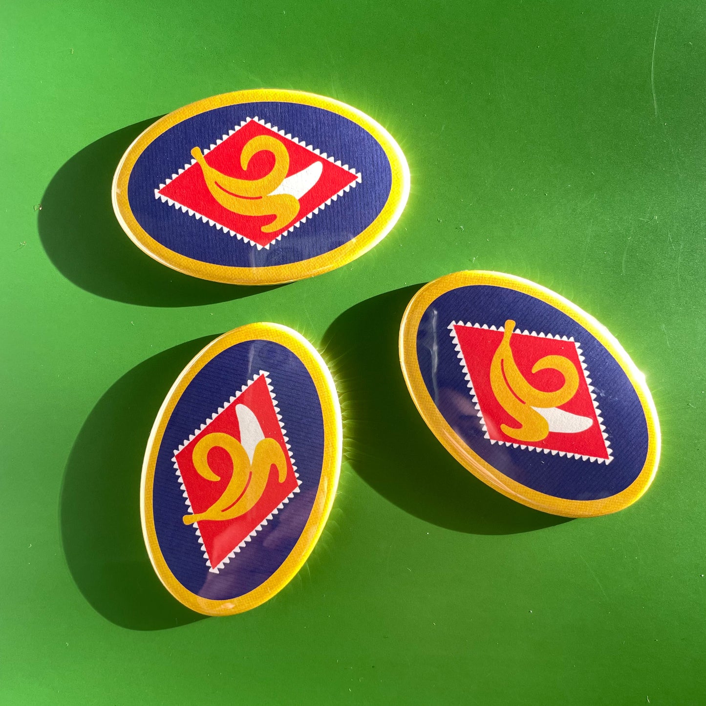 Three oval-shaped magnets with a red and yellow banana design on a green background
