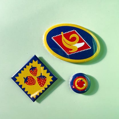 Three colorful and different shaped magnets with fruit designs on a light green background