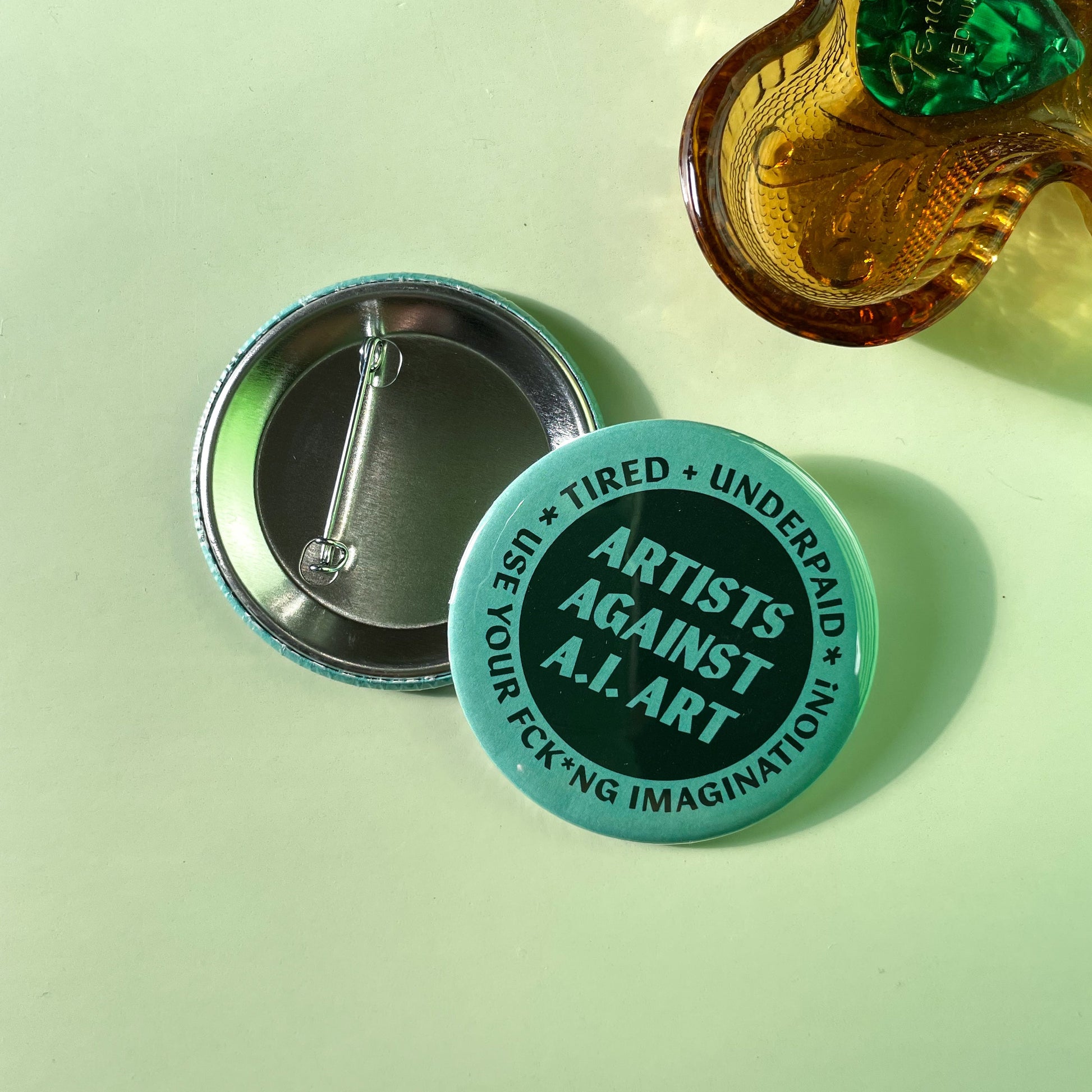Button badge with 'Artists Against AI Art' text on a light green background