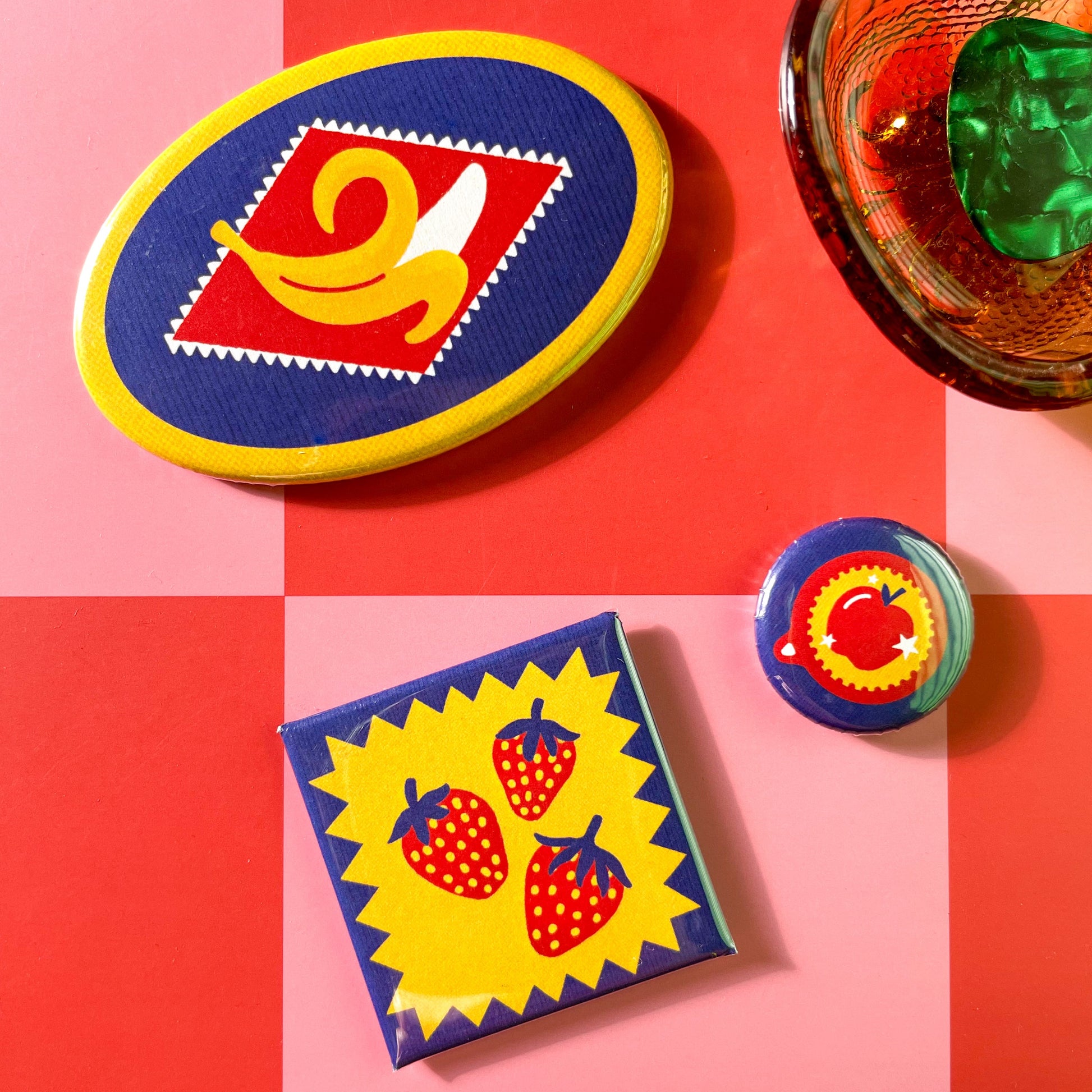 Colorful magnets with fruit themed designs on a red and pink checkered background