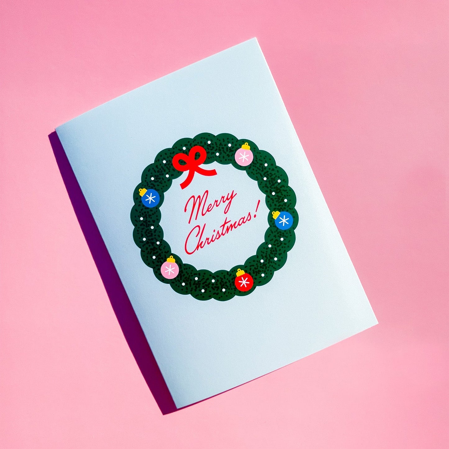 Christmas card with wreath and 'Merry Christmas' text on a pink background