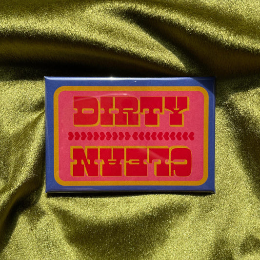 A rectangular magnet with a blue and yellow border and a pink interior. The words 'DIRTY' and 'CLEAN' are in red, bold, capital letters. Between the words are rows of red hearts. The magnet is on a green, textured surface.