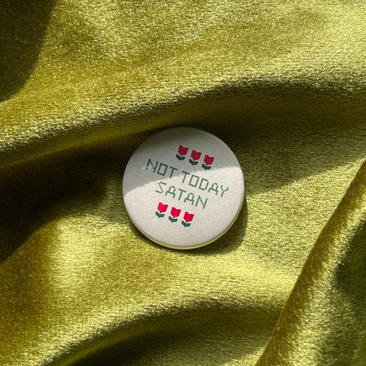 Button with 'Not Today Satan' text in a cross-stitch style and red tulips on a green fabric background